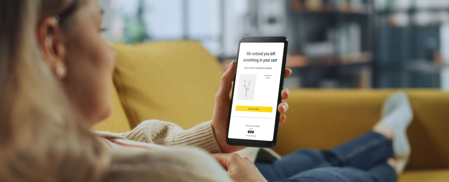 a woman sitting on a couch, receiving an abandoned cart email on her smart phone.